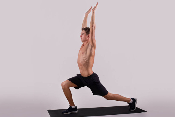 Healthy lifestyle and wellbeing. Flexible young guy doing yoga or pilates exercises on light studio background - Photo, Image