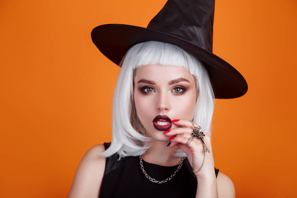 Halloween sexy witch portrait with dark lips and white hair on orange background. - Photo, image
