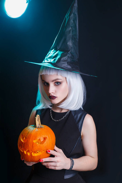 Beautifulsexy woman in witch hat and costume holding carved pumpkin. Happy halloween - Zdjęcie, obraz