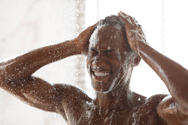 Musta mies pesu pää ja kehon suihkussa kylpyhuoneessa - Valokuva, kuva