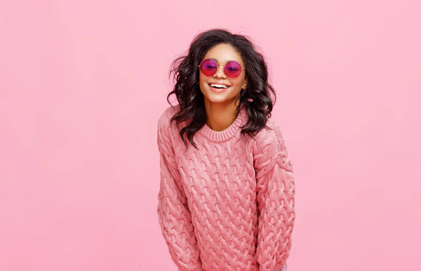 Allegro giovane femmina etnica in maglia maglione e occhiali da sole alla moda ridere contro backgroun rosa - Foto, immagini