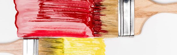 top view of paintbrushes near colorful red and yellow paint brushstrokes on white background, panoramic shot - Photo, Image