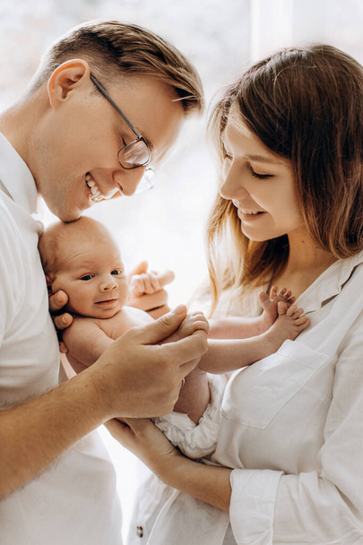Happy young parents with newborn baby girl, loving mom hold little daughter in arms, caring dad gently hold a hand of adorable baby girl, tender family moments, parenting concept - Foto, Imagem