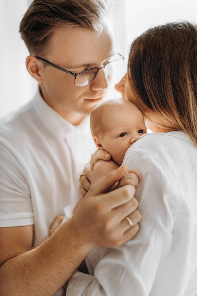Beautiful parents with newborn baby, loving mom hold little daughter in arms, caring dad gently hold a hand of adorable baby girl, enjoy tender family moments, parenting concept - Zdjęcie, obraz