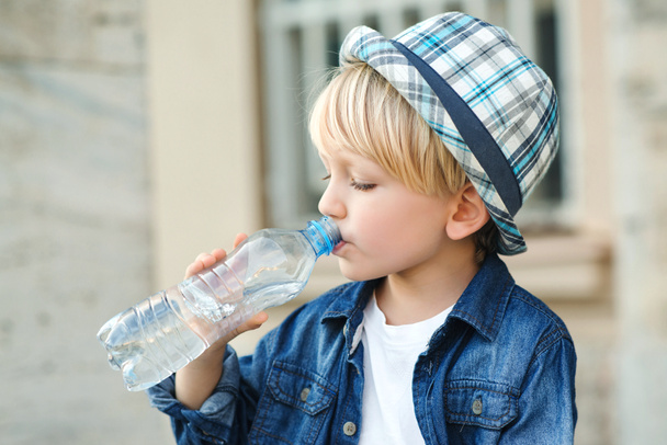 Söpö poika juo vettä muovipullosta. Lapsi juo vettä ulkona. Poika juo kivennäisvettä kadulla. Terve lapsuus. - Valokuva, kuva