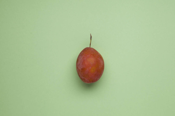 Unripe plum or prune on a green background. Flat lay, top view, copy space. - Фото, изображение