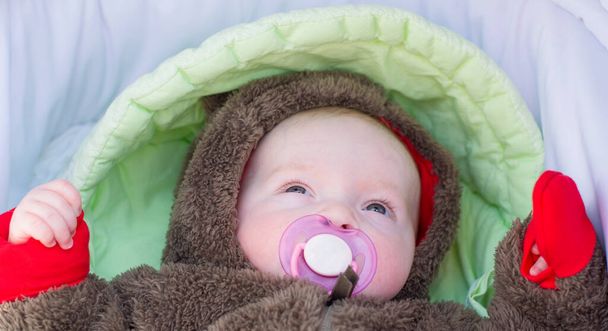 Egy kisgyerek egy mellbimbóval a szájában fekszik egy babakocsiban.. - Fotó, kép