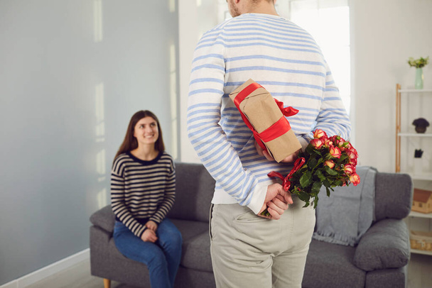 Valentines day. Rear view of a man holding flowers and gives a girl a gift in his hands - Fotó, kép