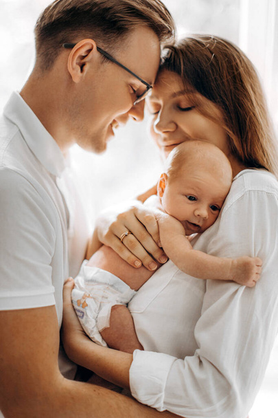Beautiful parents with newborn baby girl, loving mom hold little daughter in arms, caring husband gently hug adorable wife, smiling, enjoy tender family moments, parenting concept - Фото, изображение