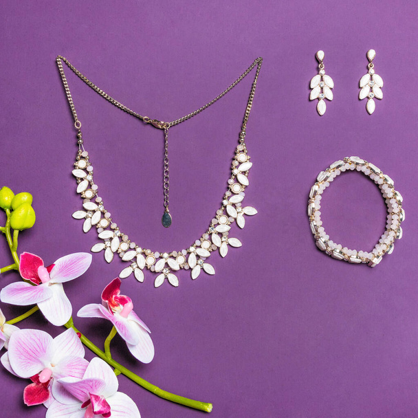 Elegante brazalete de oro y pendientes con diamantes sobre fondo púrpura - Foto, imagen