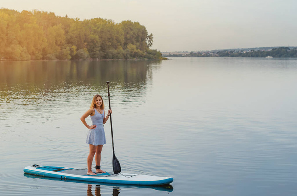 Giovane donna galleggia sull'acqua del lago su tavola linfa con un remo - Foto, immagini