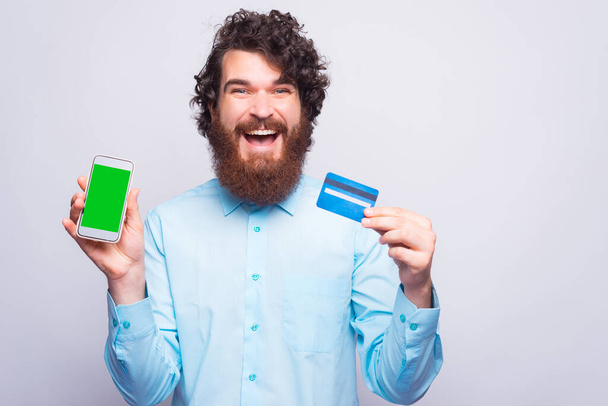 Exciting young man holding credit card and a phone looking at the camera - Foto, immagini