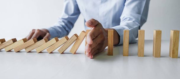 Risk and strategy in business, Close up of business woman hand stopping wooden block between three way from falling in the line of domino. - 写真・画像