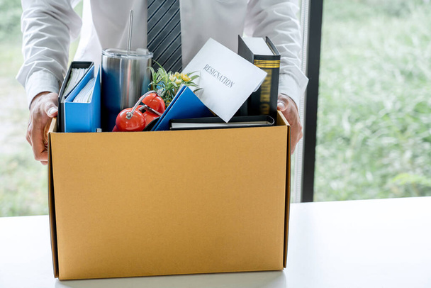 Images of businessman carrying packing up all his personal belongings and files into a brown cardboard box has frustrated and stressed to resignation and signing cancellation contract letter. - Foto, Bild