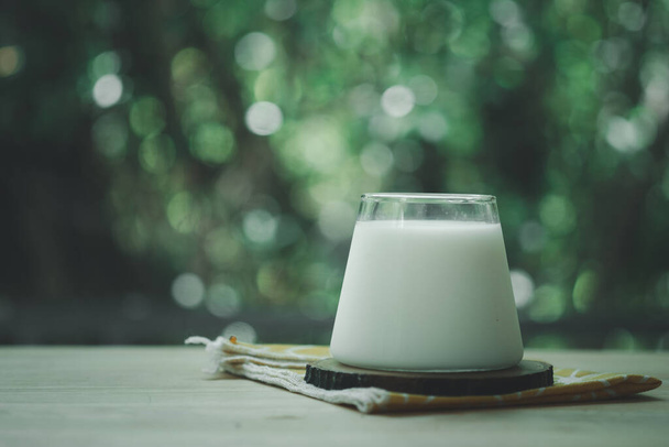木のテーブルの上にソーサーと新鮮な牛乳のガラス - 写真・画像