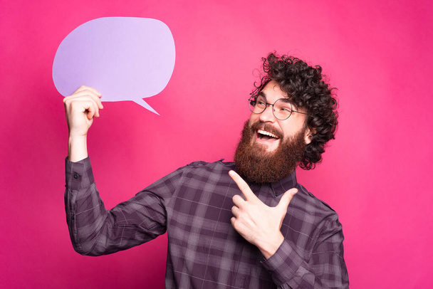 Happy young man holding a speech bubble blank and pointing at it - Photo, Image