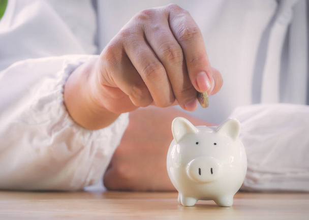Closeup of senior man hand putting coin into piggy bank to saving money for retirement financial and pension annuity insurance. Concept for loan,property,financial,estate investment,taxes and bonus. - Fotó, kép