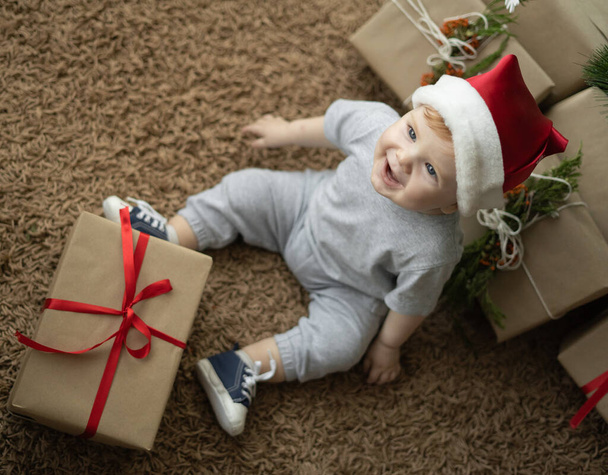 vista superior de un niño en un sombrero de santa se sienta en el suelo cerca del árbol de Navidad. Navidad invierno vacaciones concepto - Foto, imagen