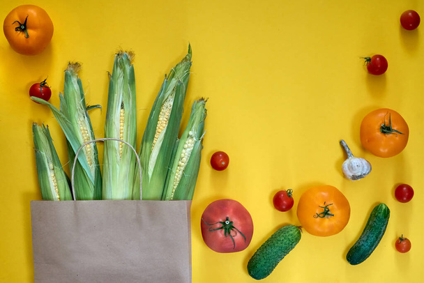 Paper craft bag with different groceries on yellow background. Top view cherry tomatoes, cucumbers, garlic. Corn harvest farm shop, fresh vegan green food delivery. - Foto, Imagem