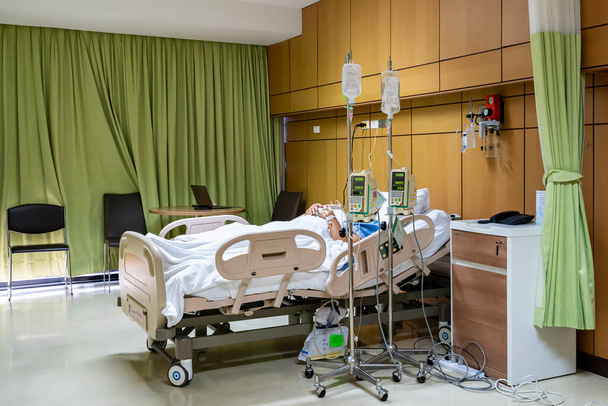 pacjent spał na łóżku był leczony roztworem soli fizjologicznej lub solą fizjologiczną przechodzącą automatyczną pompę infuzyjną zawieszoną na stojaku do wlewów dożylnych leków lub składników odżywczych w pokoju w szpitalu - Zdjęcie, obraz