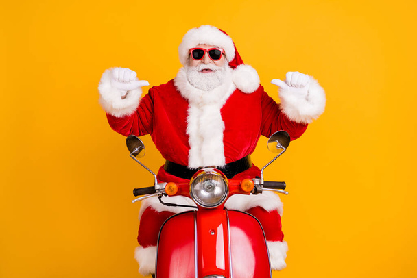 Portrait of his he nice confident cheerful Santa riding moped pointing at himself St Nicholas December tradition isolated bright vivid shine vibrant yellow color background - Фото, изображение
