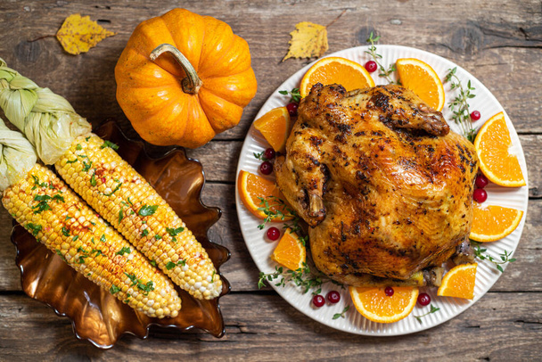 Thanksgiving autumn compositions. Roasted chicken or turkey with citrus and spices, corn for celebrations thanksgiving day on wooden table. Festive table settings for thanksgiving dinner. Top view - Photo, Image