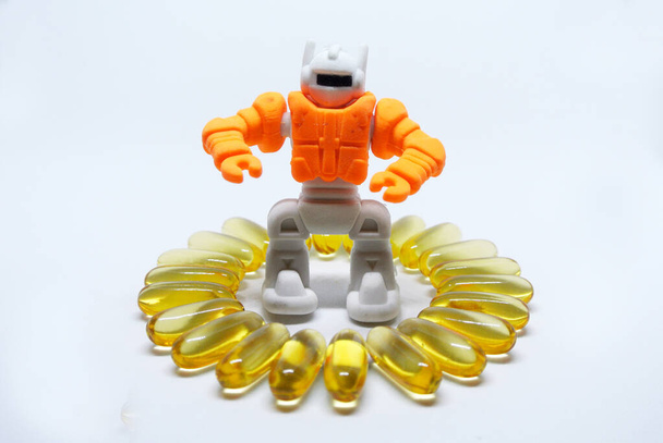 白い背景に隔離された中にゴム製のオレンジ色のおもちゃのロボットで作られた魚油カプセル - 写真・画像