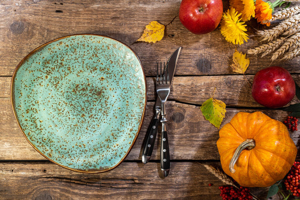 Thanksgiving background. Autumn table setting for Thanksgiving day party or festive dinner. Plate, cutlery, pumpkin, corn, floral, fruits and seasonal decoration on rustic wooden table - Photo, Image