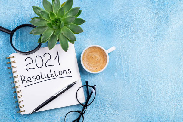 Uusi vuosi päätöslauselmat 2021 pöydällä. 2021 maalia muistikirja, kahvikuppi ja silmälasit sinisellä pohjalla. Tavoite, suunnitelma, strategia, toiminta, idea käsite. Kopioi tila - Valokuva, kuva