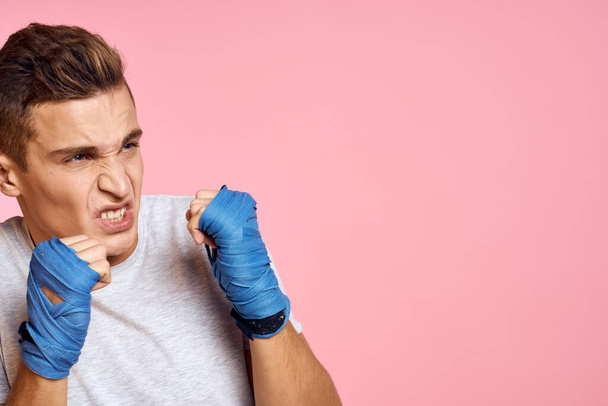 Guy in blue gloves on a pink background are boxing in a white t-shirt cropped view - Фото, изображение