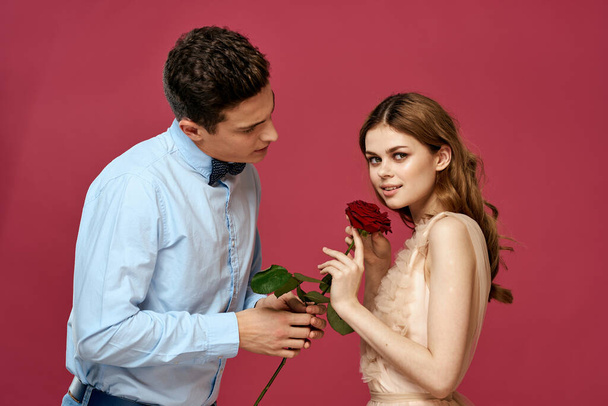 ερωτευμένοι άντρας και γυναίκα με ένα κόκκινο λουλούδι σε ροζ φόντο αγκαλιάζονται. - Φωτογραφία, εικόνα