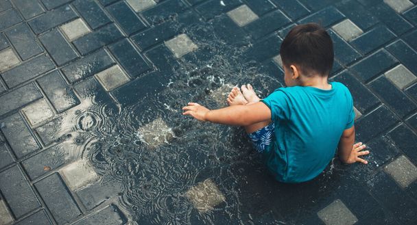 Foto vista superior de um menino caucasiano brincando na água no chão usando roupas azuis em um dia de verão - Foto, Imagem