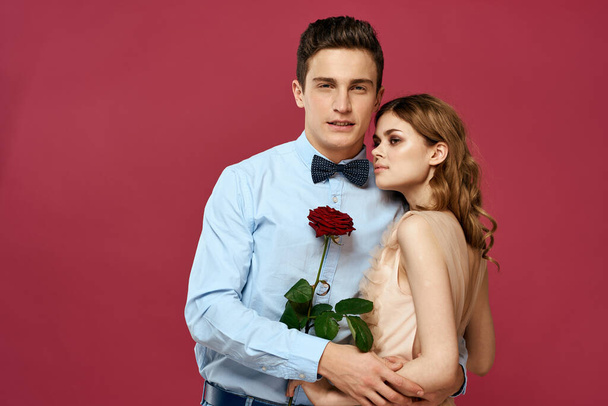 влюблённые мужчина и женщина с красным цветком на розовом фоне обнимают друг друга - Фото, изображение