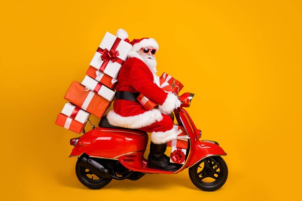 Profile side view of his he nice funny fat white-haired Santa riding moped fast speed hurry up rush carrying bringing pile stack giftbox isolated bright vivid shine vibrant yellow color background - Zdjęcie, obraz