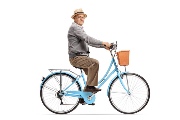 Anciano montando una bicicleta azul y sonriendo a la cámara aislado sobre fondo blanco - Foto, imagen