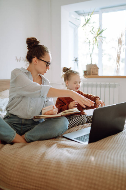 Mom working remotely on laptop while taking care of her baby. Young mother on maternity leave trying to freelance  with daughter. Stay at home. Covid-19. - Fotoğraf, Görsel