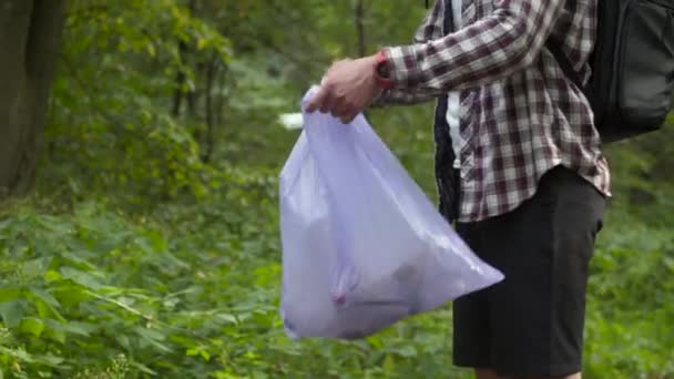 Плохой человек выбрасывает мусор из пластикового мусорного пакета в лесу. Мужчина оставляет мусор и уходит. Загрязнение и экологическая проблема, переработка пластмасс, загрязнение природы - Кадры, видео