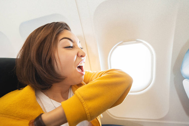 female airplane passenger sneezes into her elbow. First signs of corona virus and covid-19 infection during air transportation - 写真・画像