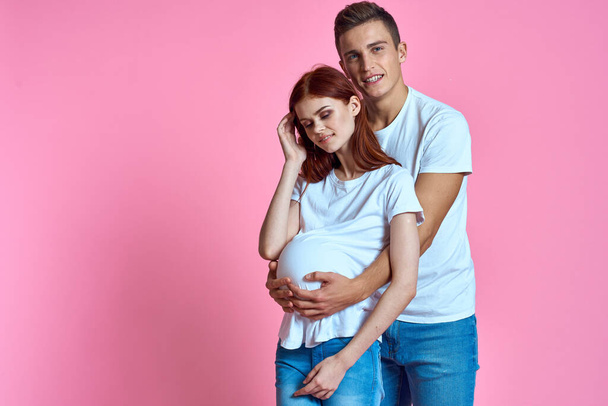 madre embarazada y padre feliz sobre fondo rosa Joven familia esperando al bebé - Foto, imagen