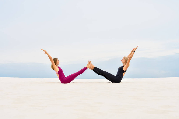 Dos hermosas mujeres jóvenes realizan pose de yoga navasana - Foto, Imagen