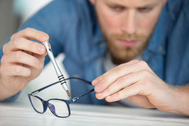 optician repairing broken glasses in workshop - 写真・画像