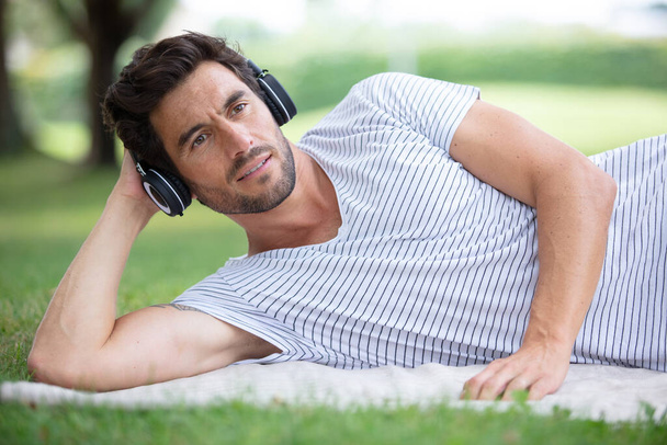 carefree man lying on the grass and listening music - Photo, Image