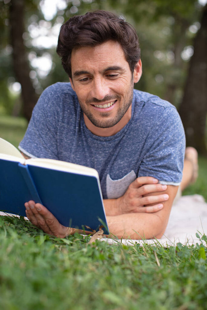 man lying in the grass relaxing and reading a book - Photo, Image