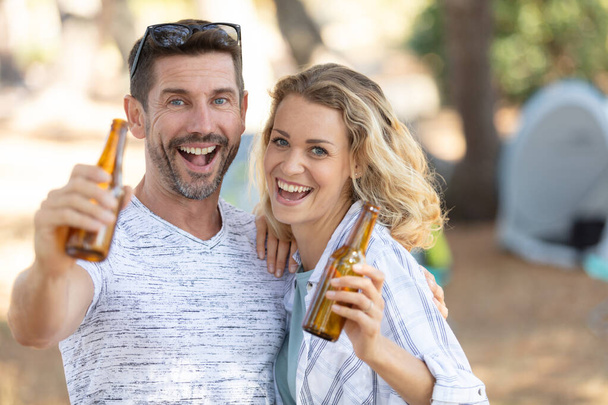 happy couple clinking beer bottles at campsite tent - Photo, image