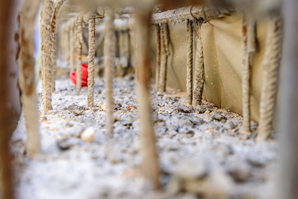 Detail van stalen staven in cement voor het gewapend beton van de funderingen van een muur van een gebouw in aanbouw, met niet-gerichte achtergrond. - Foto, afbeelding