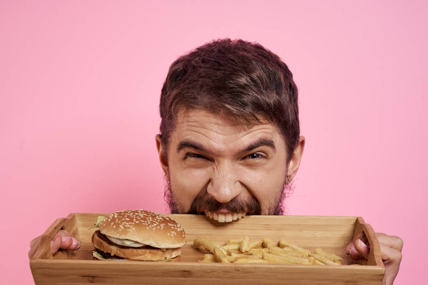 Agresywny facet z tacą w ręku hamburger frytki różowy tło głodny wygląd - Zdjęcie, obraz
