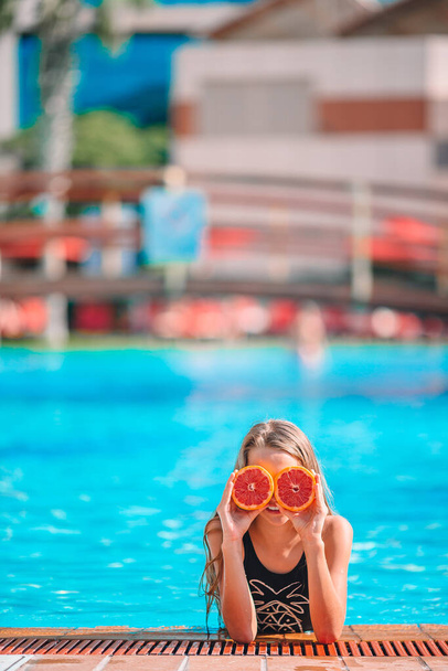 Menina cobrindo os olhos com metades de laranja perto de olhos na piscina de fundo - Foto, Imagem