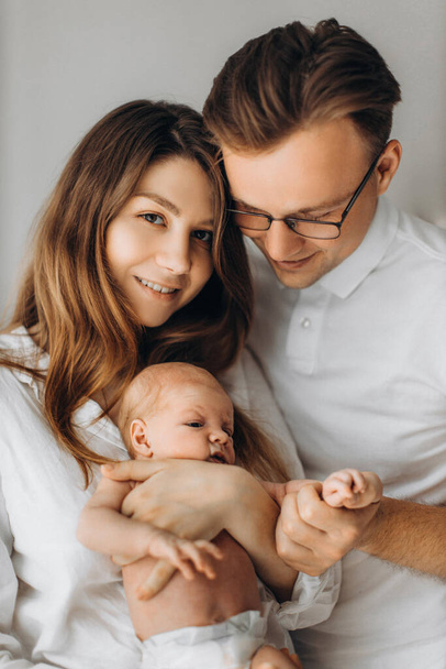 Portrait of parents with newborn baby, loving mom gently hold little daughter in arms, caring dad hold tiny hand of baby girl, smiling, enjoy happy moments, young family concept - Photo, image