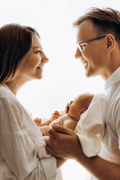 Happy young family with little daughter, beautiful mother hold cute newborn baby in arms, caring father hold hands of adorable baby girl, mom and dad smiling, parenting concept - Foto, imagen