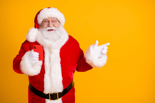 Excited santa claus with big belly use cellphone search x-mas magic fairy christmas eve discount ads point finger copyspace wear cap headwear belt isolated bright shine color background - Foto, afbeelding